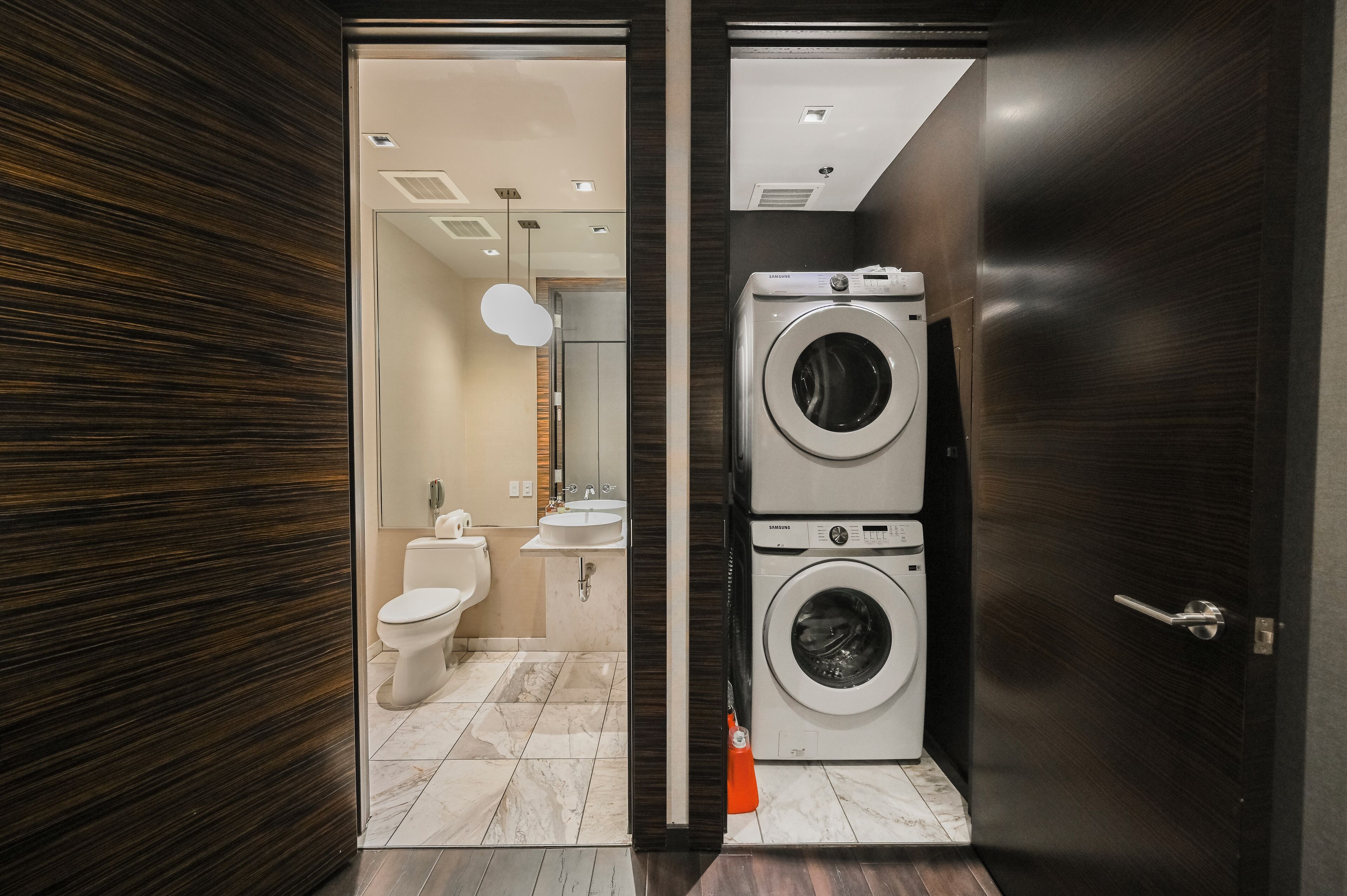 A compact bathroom with a toilet, sink, and stacked washing machines.