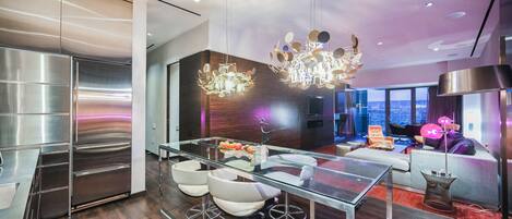 A modern kitchen with stainless steel appliances, a glass dining table with bar stools, and a contemporary chandelier.