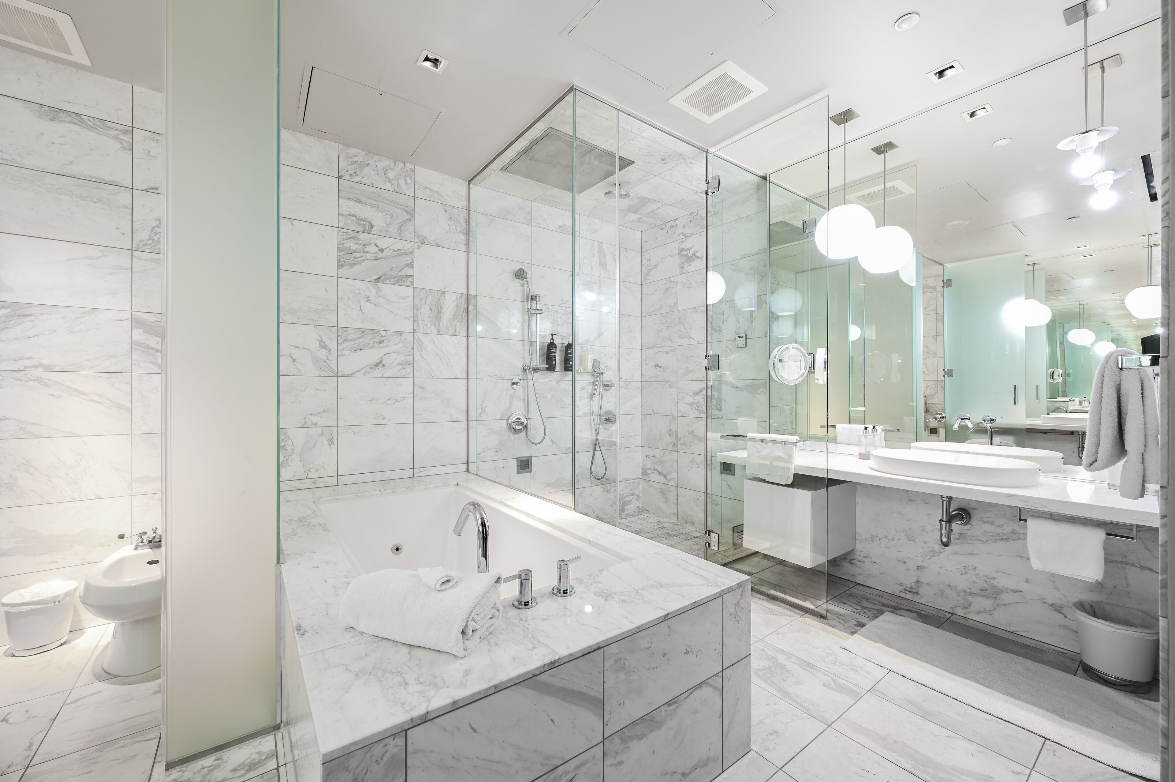 A modern bathroom with a glass-enclosed shower, a large marble sink, and a vanity with a mirror.