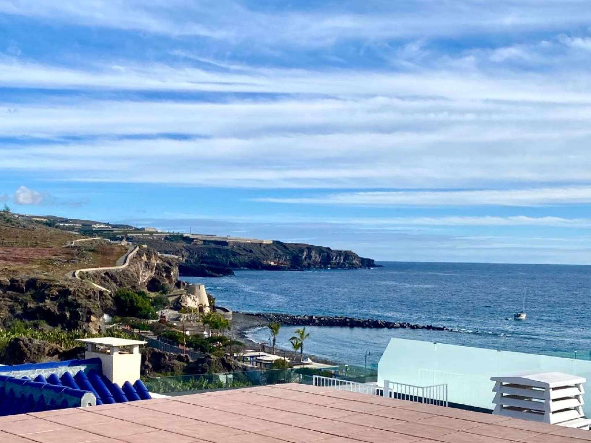A coastal view with a rocky cliff, a clear sky, and a calm sea.