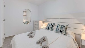 Un dormitorio con una cama, una mesita de noche, un ventilador de techo y un espejo fijado a la pared.