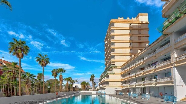 Un hotel con una piscina grande, varios balcones y palmeras.