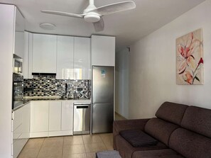 A compact kitchen with white cabinets, a stainless steel refrigerator, and a tiled backsplash.