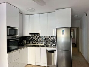 Eine kleine Küche mit weißen Schränken, einer Mikrowelle, einem Backofen, einem Geschirrspüler und einer gefliesten Spritzschutzwand.