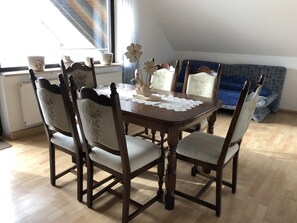 A dining area with a wooden table and chairs, a lace tablecloth, and a window with curtains.
