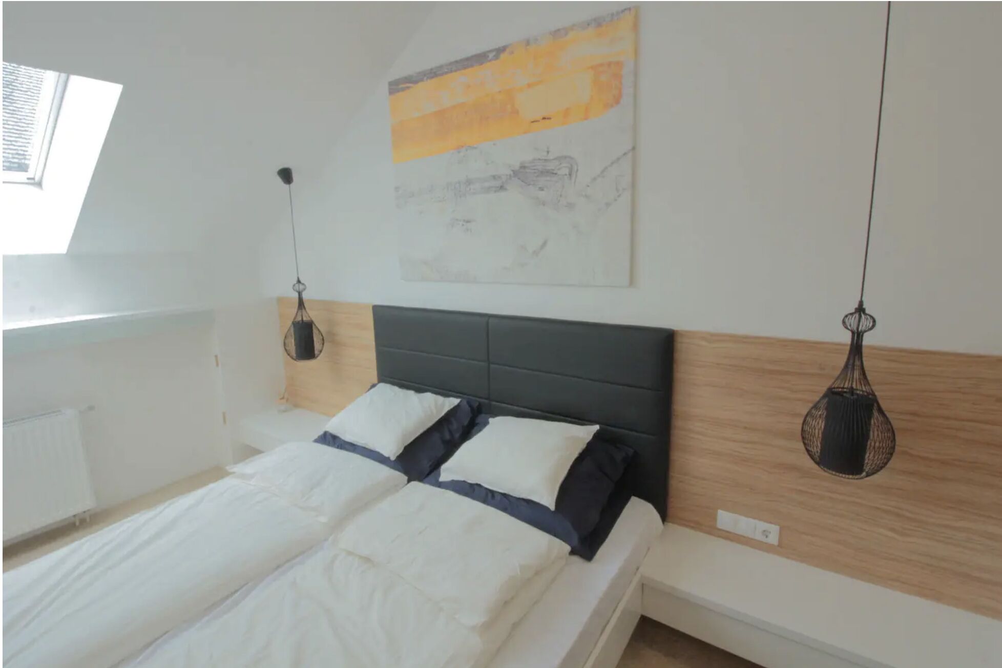 A bedroom with a bed, a window, and a painting on the wall.