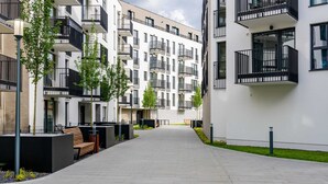 Un edificio de apartamentos moderno con balcones, un sendero pavimentado y mobiliario exterior.