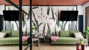 Una sala de estar moderna con un sofá verde, una mesa de comedor con sillas y un gran mural en la pared con aves.