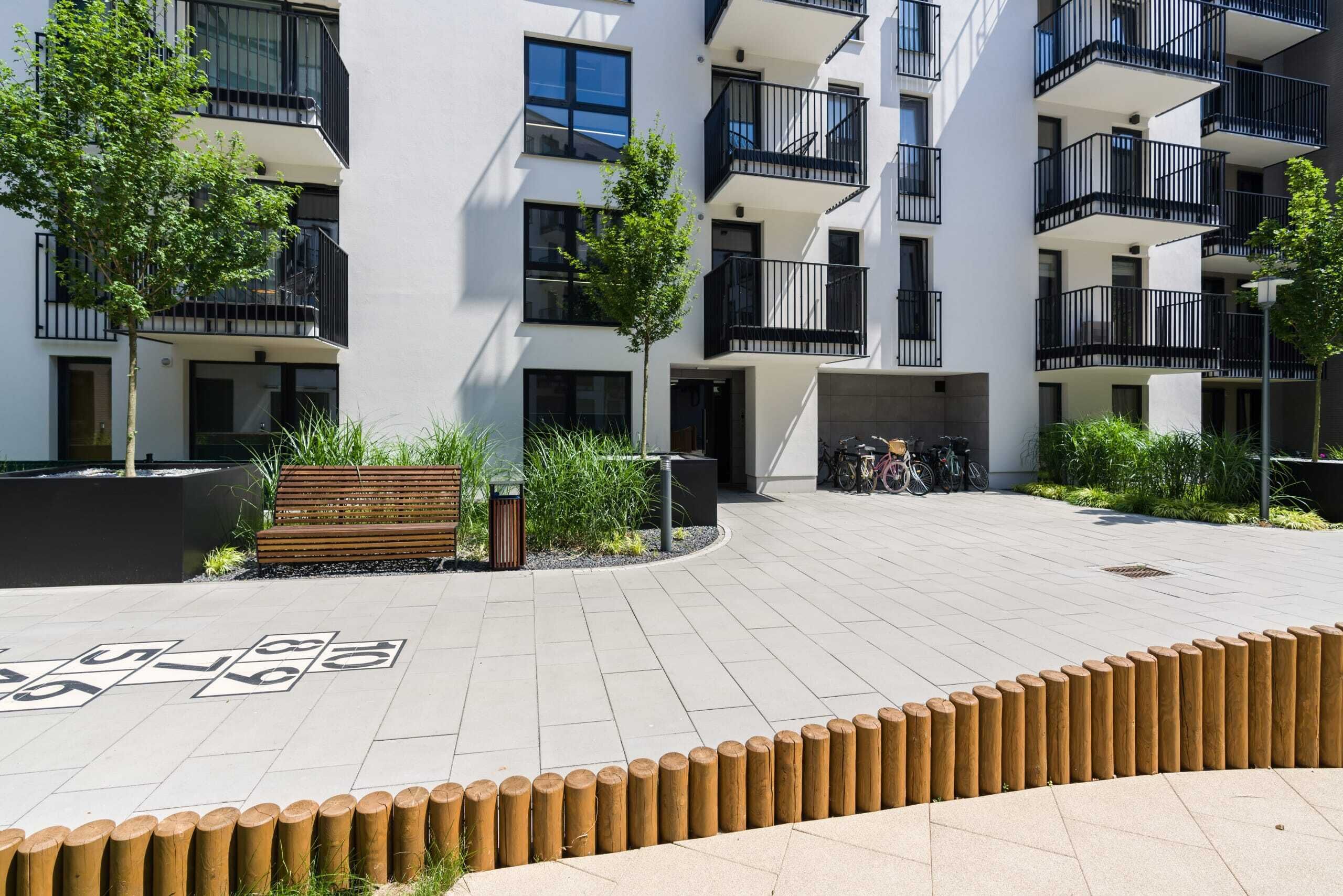 Un immeuble d’appartements moderne doté de balcons, d’une cour pavée et d’un vélo garé à l’extérieur.