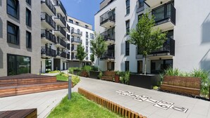 Un moderno complejo de apartamentos con varios balcones, un patio central con un juego de rayuela y bancos de madera.
