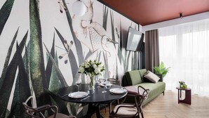 Un comedor con una mesa redonda dispuesta para cuatro personas, rodeada de sillas. Se ve un sofá y una pequeña mesita con una planta al fondo.