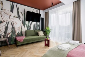 A modern hotel room with a green sofa, a flat-screen TV, a potted plant, and a bed with folded towels. - Stylish Studio in the Center | Balcony | Close to the Old Market (Poznan)