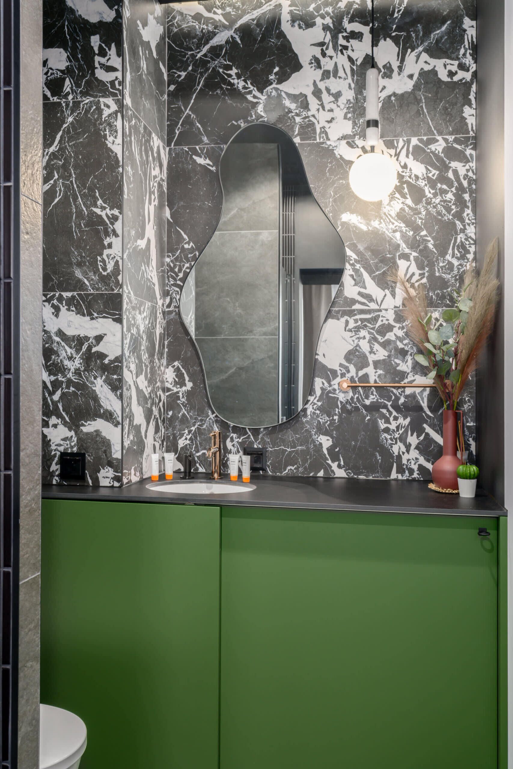 Un baño con salpicadero de mármol, un lavamanos moderno y un armario verde.