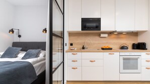 A modern bedroom with a bed, bedside table, and a nightstand. Adjacent to the bedroom is a compact kitchenette with a stove, sink, and countertop. - Cozy Apartment with Terrace | Private Parking, Close to Airport (Gdańsk)