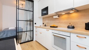 A compact kitchen with white cabinets, a wooden countertop, a microwave, an oven, and a sink. - Cozy Apartment with Terrace | Private Parking, Close to Airport (Gdańsk)