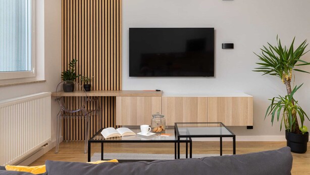 A modern living room with a flat-screen TV mounted on the wall, a glass coffee table, a sofa, and a wooden accent wall. - Cozy Apartment with Terrace | Private Parking, Close to Airport (Gdańsk)