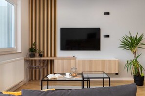 Una sala de estar moderna con una televisión de pantalla plana montada en la pared, una mesa de centro de vidrio, un sofá y una pared de acento de madera.