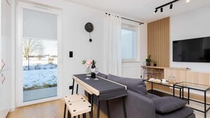 A modern living room with a grey sofa, a small table with a vase, and a TV mounted on the wall. - Cozy Apartment with Terrace | Private Parking, Close to Airport (Gdańsk)