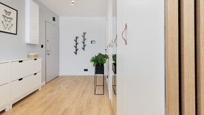 A modern hallway with a wooden floor, white walls, a white cabinet with drawers, a framed butterfly artwork, a door, and two black wall-mounted plants. - Cozy Apartment with Terrace | Private Parking, Close to Airport (Gdańsk)