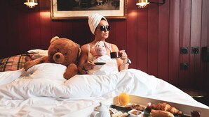A person sitting on a bed with a teddy bear and a cup, with breakfast items on the side. - Naâd Hotel (Sarlat-la-Canéda)
