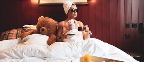 A person sitting on a bed with a teddy bear and a cup, with breakfast items on the side.