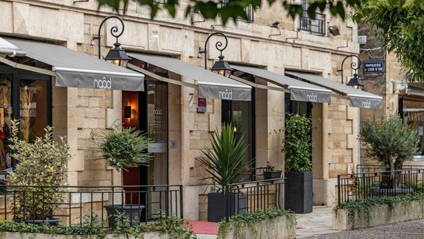 A row of outdoor cafe umbrellas with the 'naod' logo, stone building facade, and potted plants. - Naâd Hotel (Sarlat-la-Canéda)