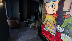 A modern hotel lobby with a large colorful mural, a brown leather armchair, a small round table, and a beige armchair. - Naâd Hotel (Sarlat-la-Canéda)