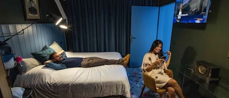 Habitación de hotel con una cama, una silla, un televisor y un reloj en la pared.