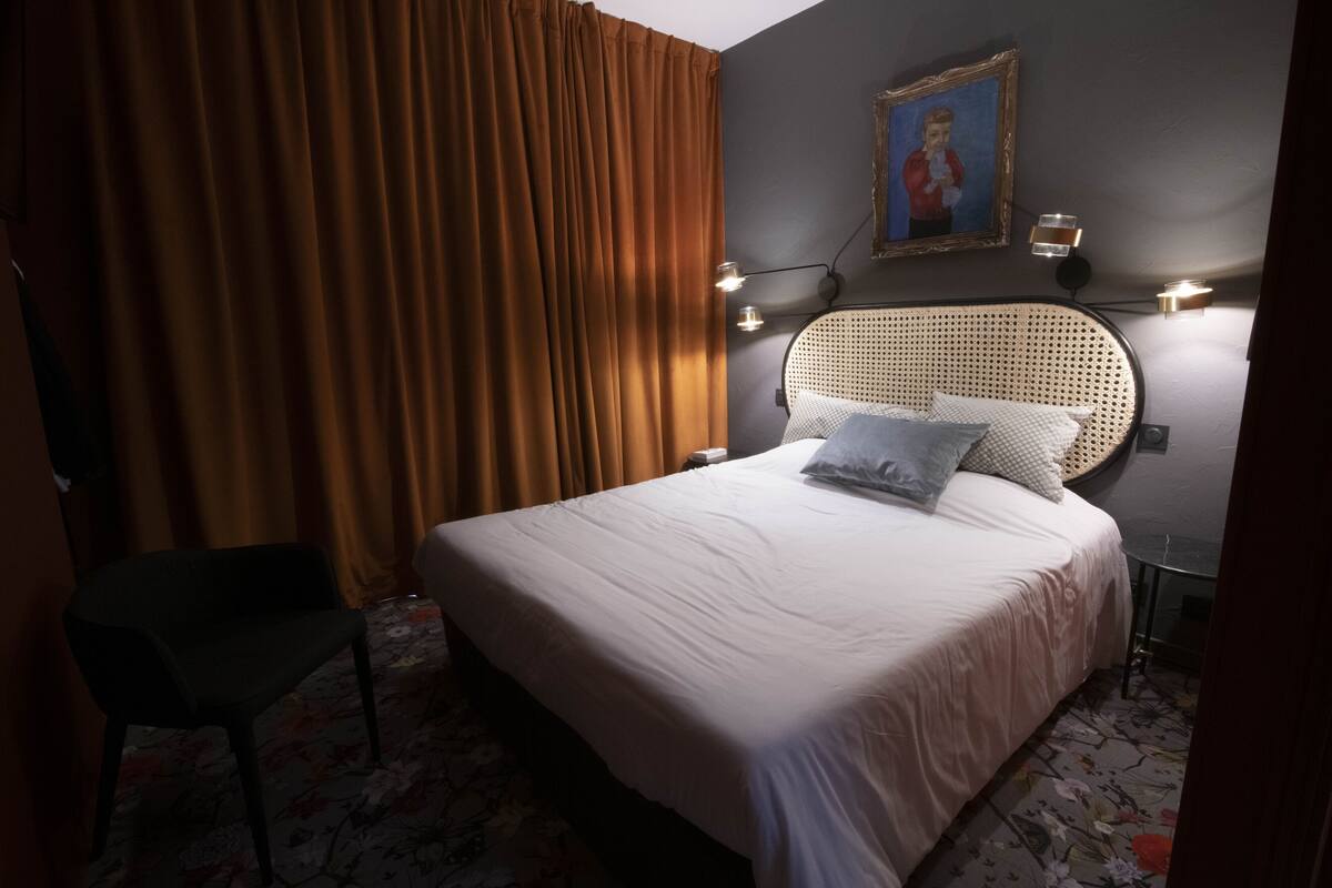 Ein Hotelzimmer mit einem großen Bett, einem Sessel, einem Bild an der Wand und zwei Wandleuchten.