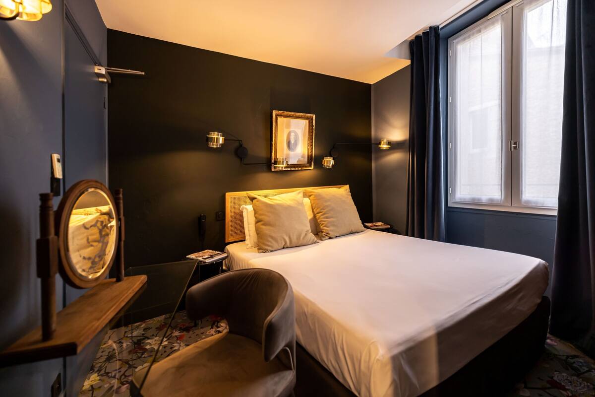 Ein Hotelzimmer mit Bett, Nachttisch, Stuhl und einem fenster mit Vorhängen.