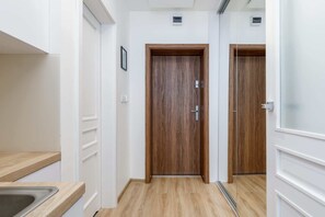 A narrow hallway with wooden doors, a light-colored floor, and a kitchen area with a sink.
