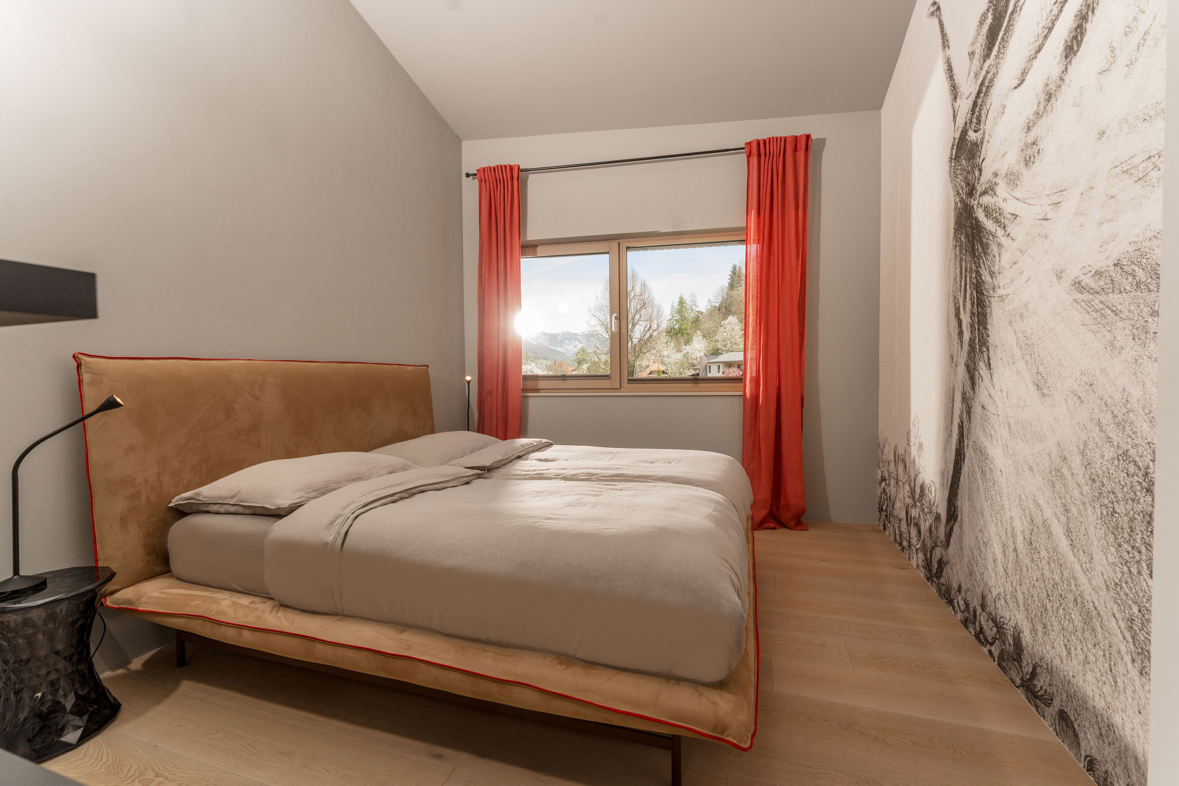 A bedroom with a bed, a nightstand, a window with curtains, and a wall with a textured mural.