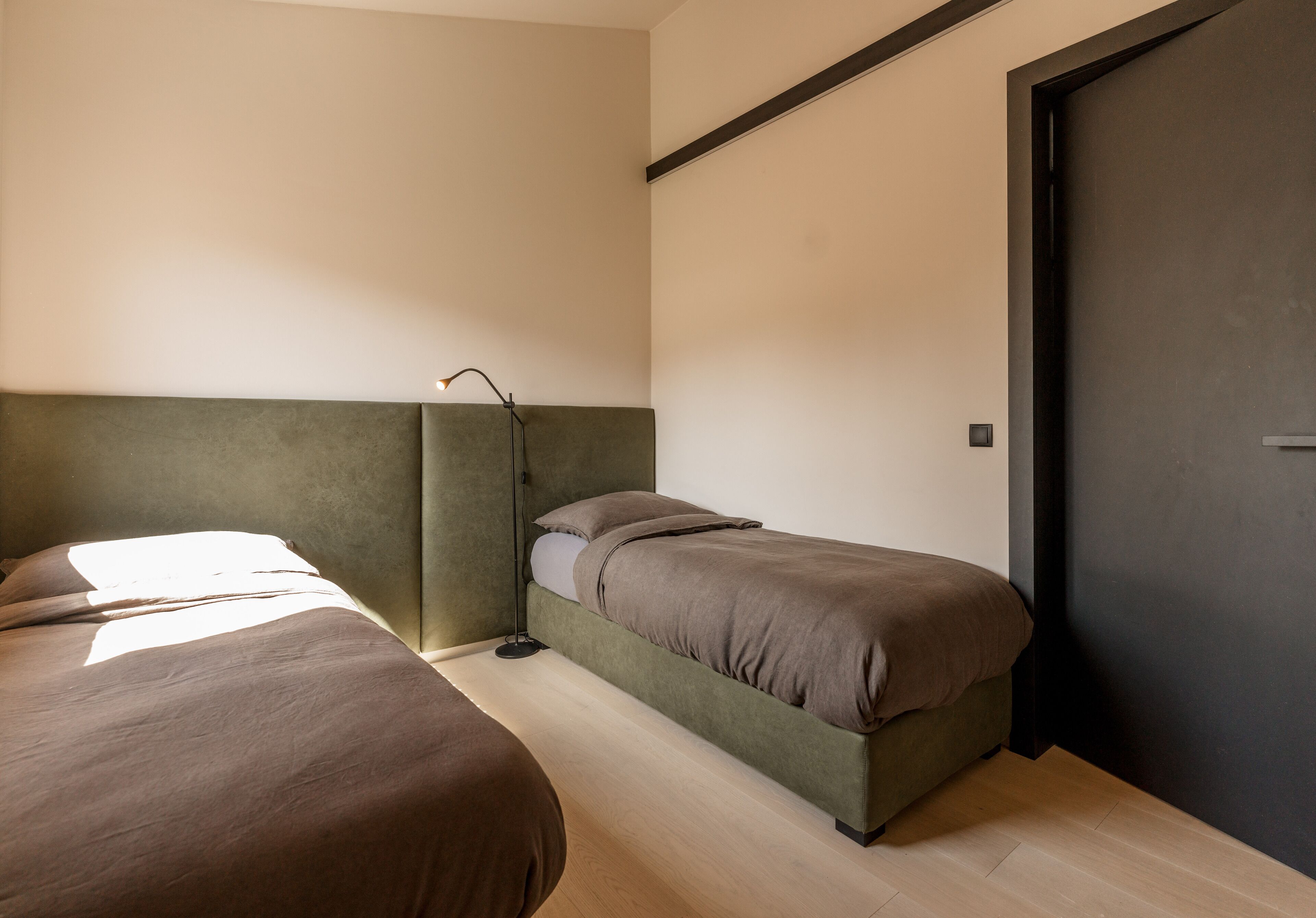 A bedroom with two beds, a bedside table, a lamp, and a door.