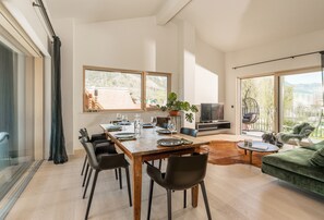 A modern living room with a wooden dining table set for four, a green sofa, and a large window offering a view of a mountainous landscape. - City Fischer Design Apartment (Schladming)