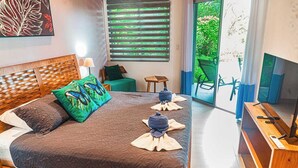 A well-lit bedroom with a large bed, a wooden headboard, a green pillow, and a view of greenery through the window. - 3 bedroom. 10 min to Beach. Private Pool. (Ojochal)