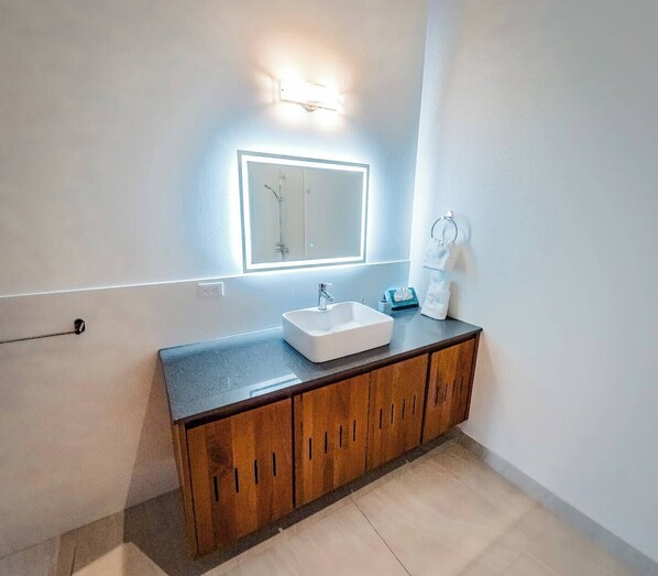 Een moderne badkamer met een rechthoekig wastafelmeubel, houten kastjes en een spiegel op de muur met ingebouwde verlichting.