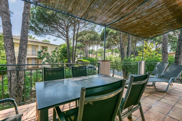 Un patio al aire libre con una mesa y sillas, rodeado de  árboles y una vista de un edificio al fondo.