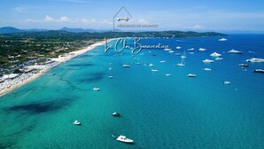 Vista aérea de una zona costera con playa, barcos y montañas al fondo.