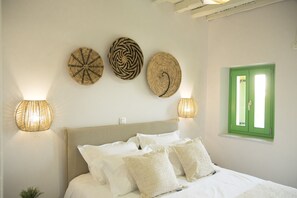 A bedroom with a bed, pillows, and wall-mounted woven decorations. - Ano Siroa. Cycladic house with amazing views (Ano Syros)