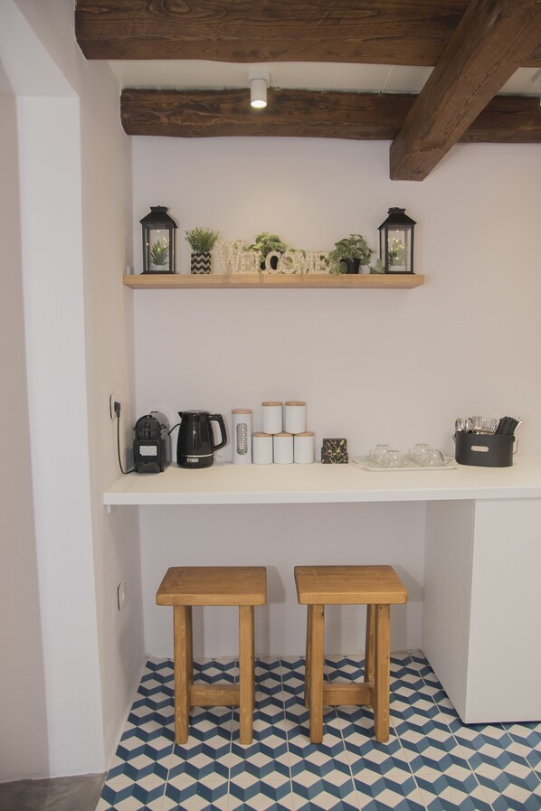 A kitchen with wooden beams, a white countertop, two stools, and patterned floor tiles. - Ano Siroa. Cycladic house with amazing views (Ano Syros)