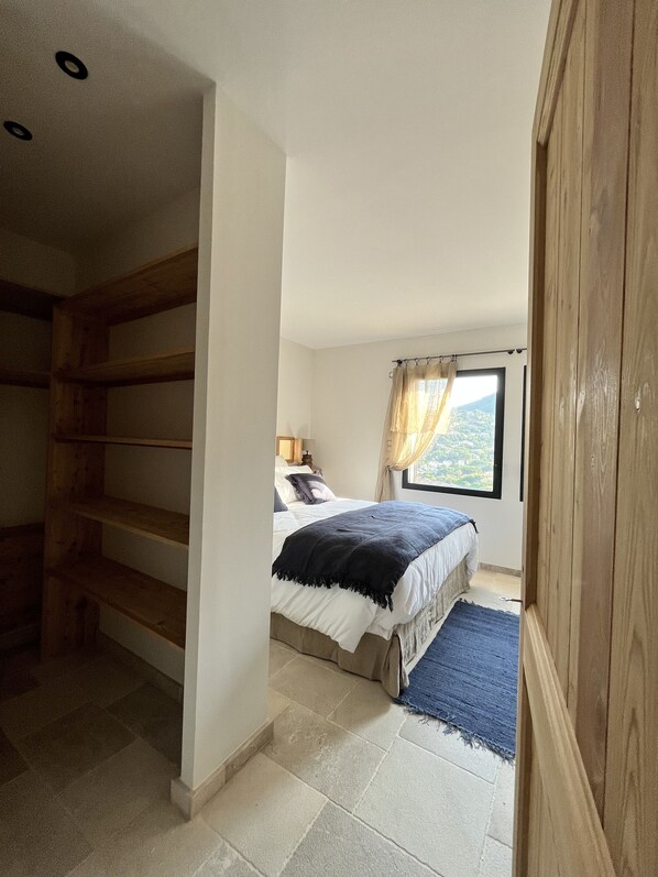 A bedroom with a bed, a window with curtains, a wooden wardrobe, and a staircase.