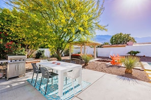Enjoy al fresco dining and relaxation in this serene outdoor space, featuring a barbecue grill, dining table, and comfortable seating under a pergola, with a pool and lounge chairs nearby.