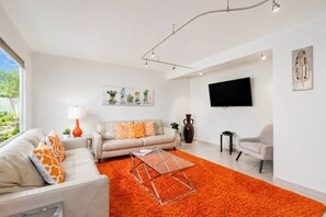 Un salon moderne comprenant un canapé, un fauteuil, une table basse et un téléviseur à écran plat.