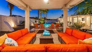 Une terrasse extérieure avec des canapés orange, une piscine et un espace abrité doté d’un ventilateur de plafond.