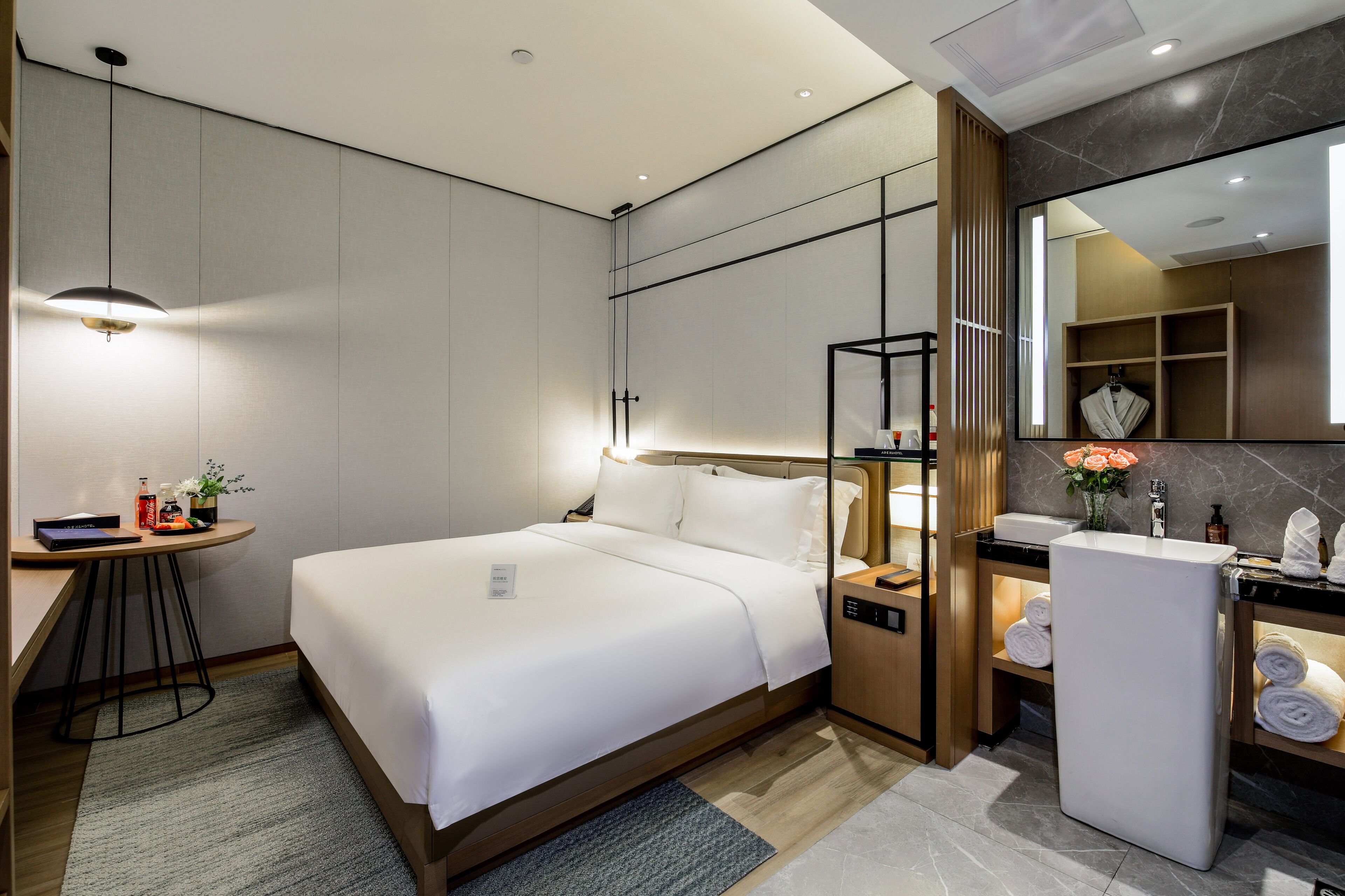 Une chambre d’hôtel moderne équipée d’un lit, d’une table de chevet, d’une lampe et d’une salle de bain avec un lavabo et un miroir.