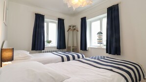 A hotel room with two beds, a hanging light fixture, and a window with a view of the beach. - Coastal Nest (Seahouses)