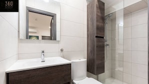 Une salle de bain moderne avec un lavabo blanc, un meuble-lavabo en bois foncé, des toilettes et une douche à parois de verre.