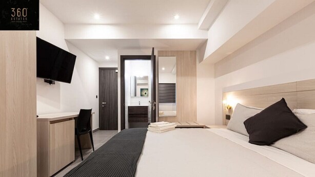 Une chambre d’hôtel moderne équipée d’un lit, d’une table de chevet et d’un téléviseur fixé au mur.