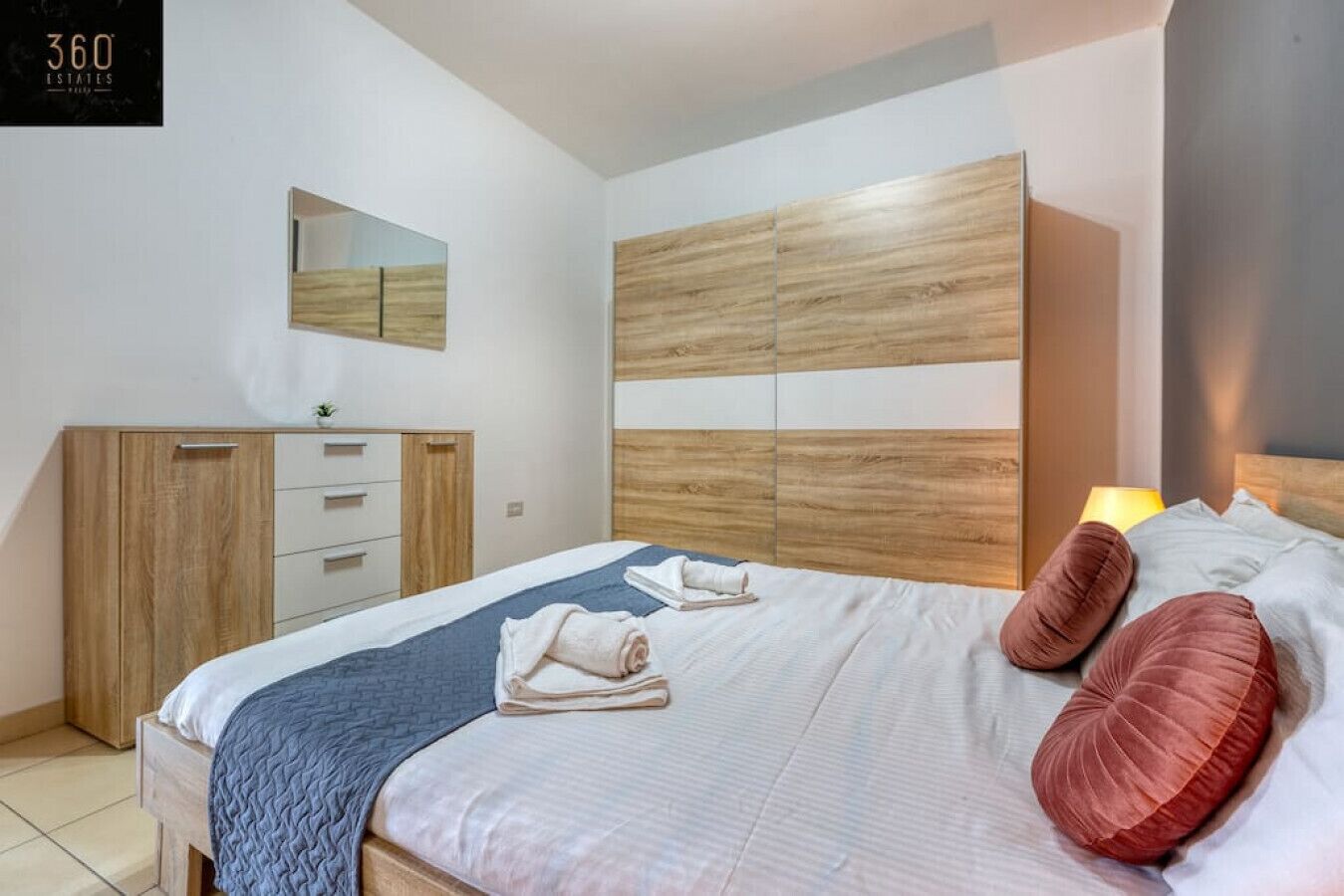 Quarto moderno com uma cama grande, cabeceira de madeira, um guarda-roupa e um espelho.