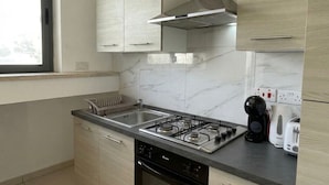 A modern kitchen with a gas stove, stainless steel sink, and light wood cabinets. - Stylish 2BR Meridian suite in central St Julians (San Ġiljan)